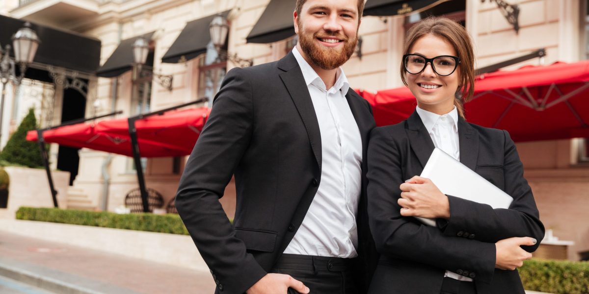 Portrait of a beautiful man and woman wearing smart clothes Portrait of a beautiful successful man and woman wearing smart clothes holding tablet computer and looking at camera while standing on a city street